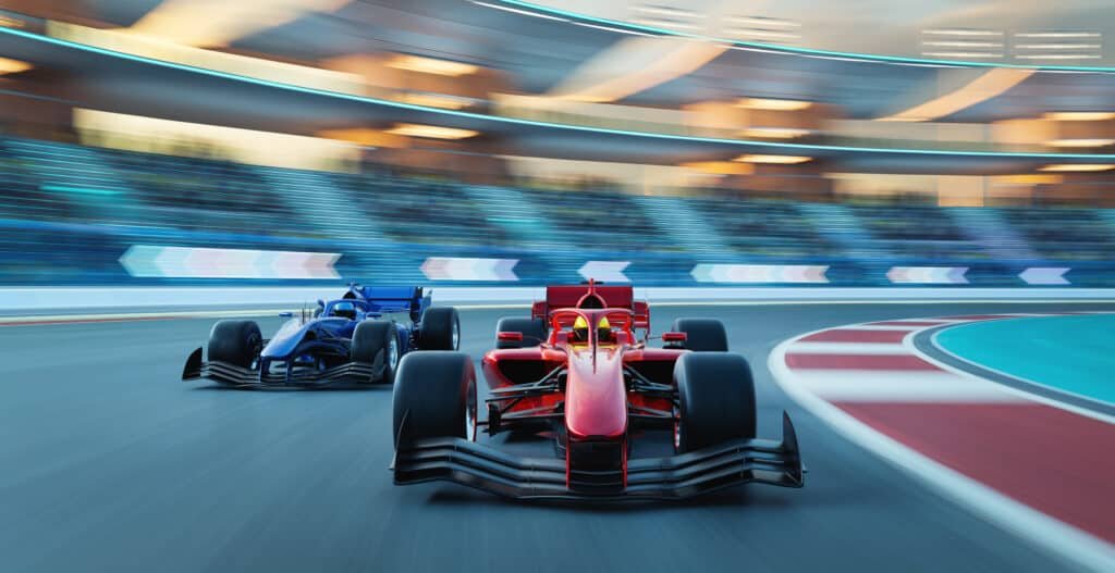 Deux monoplaces, une rouge et une bleue, lancées côte à côte dans un virage de circuit devant des tribunes