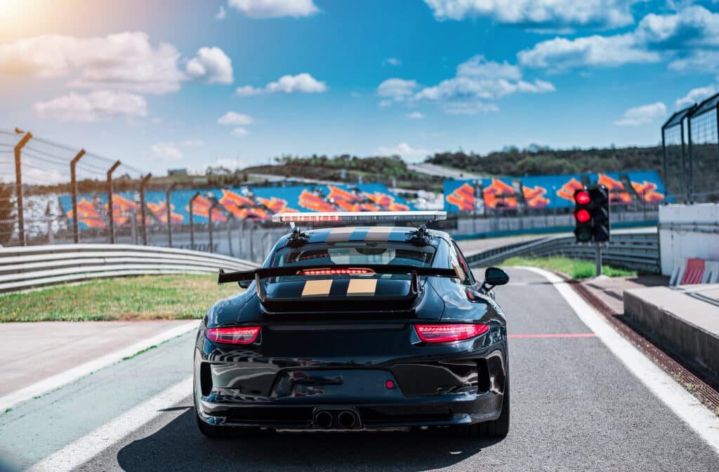 Voiture de sport noire à bandes dorées et aileron arrière, vue de dos à la sortie de la voie des stands d'un circuit