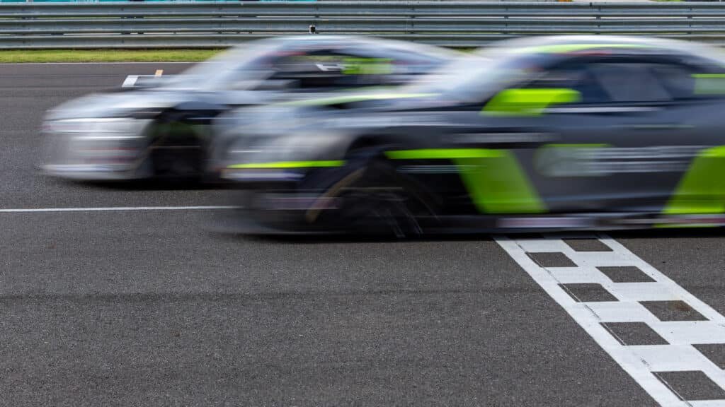 Deux voitures de course floutées par la vitesse au moment de franchir la ligne d'arrivée à damier