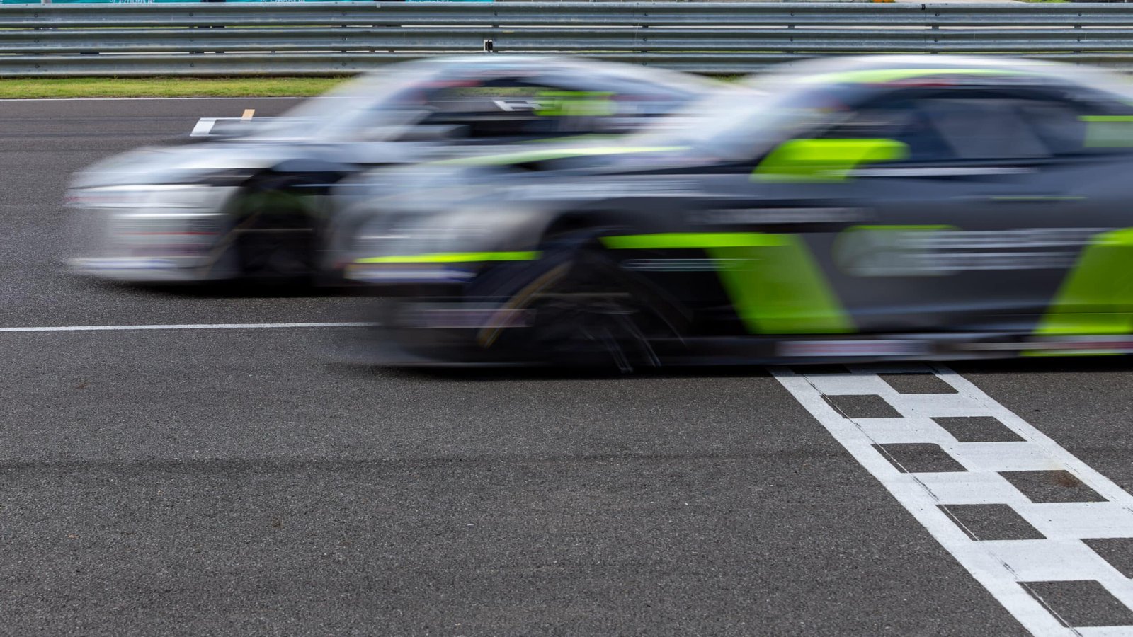 Deux voitures de course floutées par la vitesse au moment de franchir la ligne d'arrivée à damier