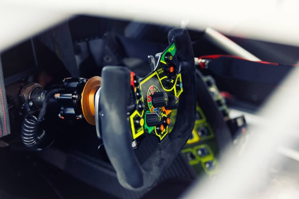 Gros plan sur le volant d'une voiture de course, moyeu à attache rapide à bague orange et câble spiralé visibles