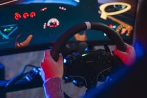 Deux mains sur la jante d'un volant simracing marquée en son sommet, tableau de bord affiché à l'écran