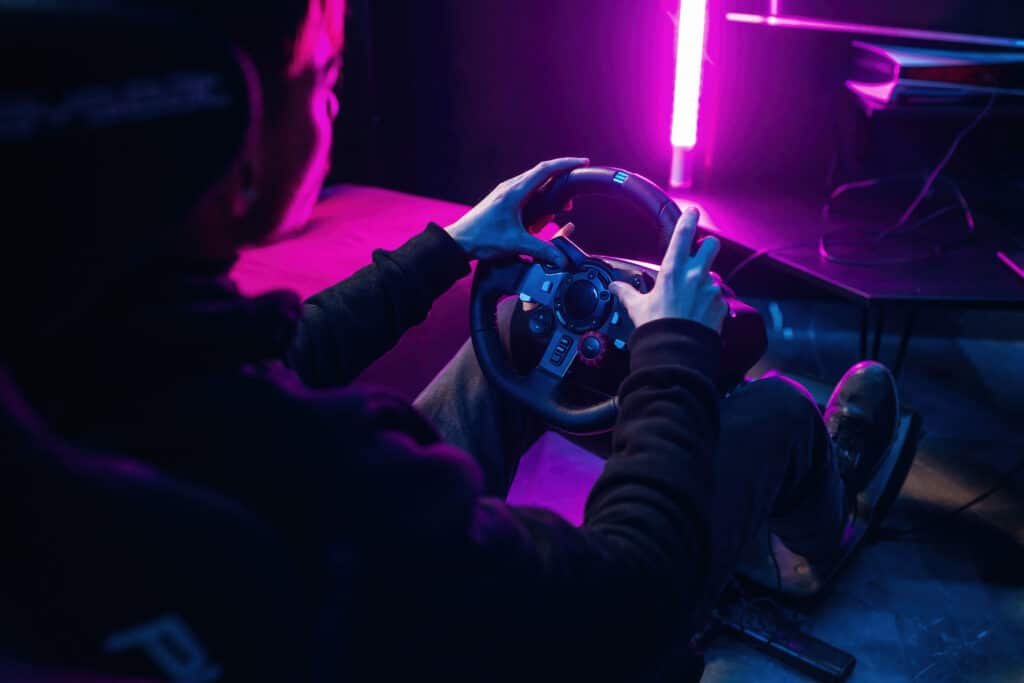 Pilote vu de dos, les deux mains sur la jante d'un volant simracing, pédalier au sol, éclairage néon violet