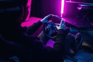 Pilote vu de dos, les deux mains sur la jante d'un volant simracing, pédalier au sol, éclairage néon violet