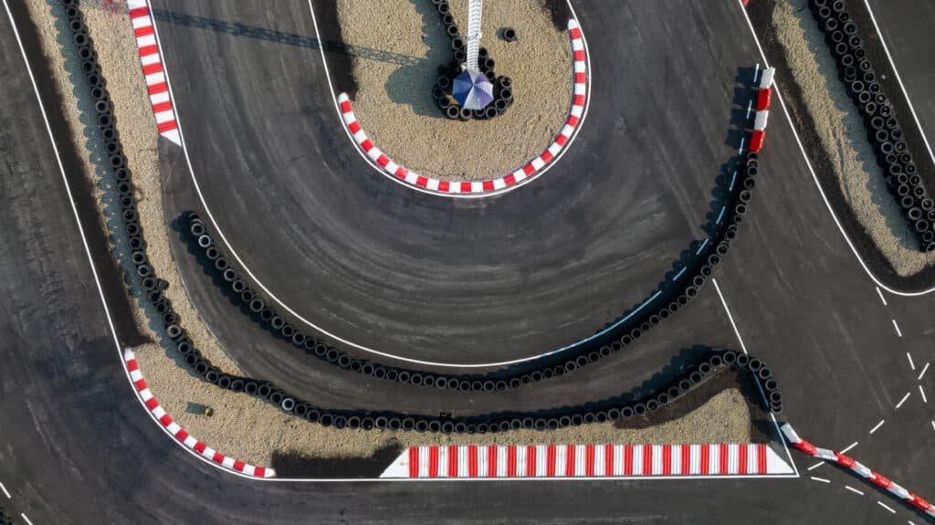 Vue aérienne d'un circuit de karting, vibreurs rouges et blancs, murs de pneus et ligne de départ