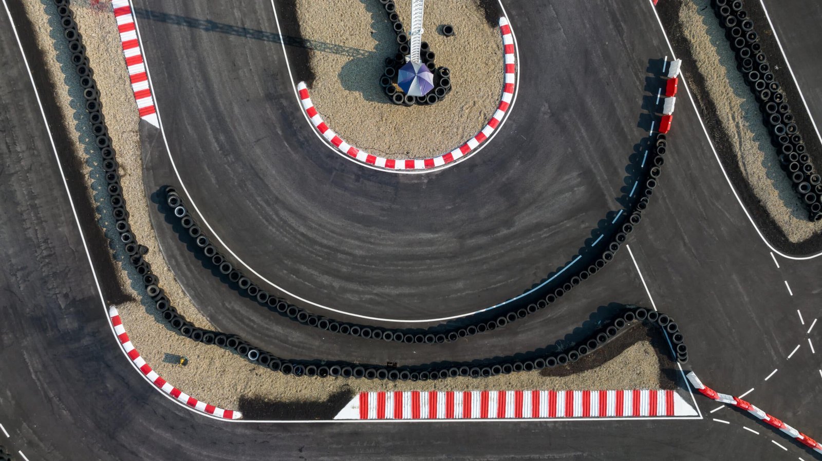 Vue aérienne d'un circuit de karting, vibreurs rouges et blancs, murs de pneus et ligne de départ