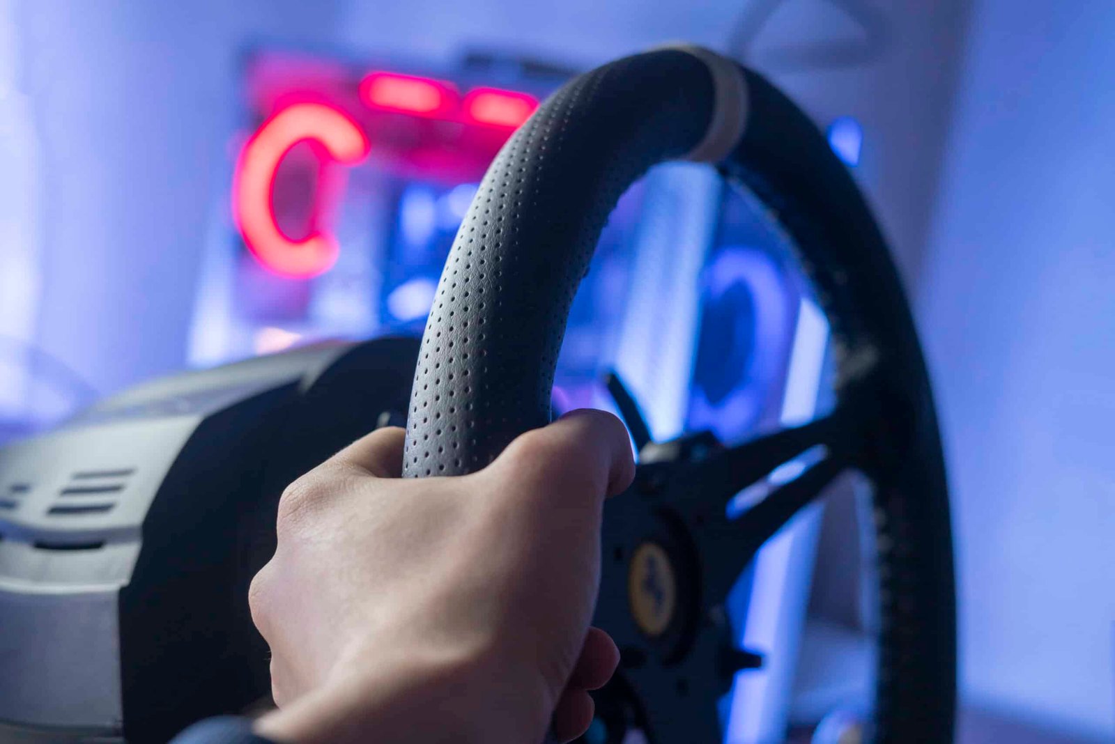 Main sur la jante perforée d'un volant simracing, repère clair visible en haut de la jante, néon rouge en arrière-plan