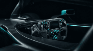 Main gantée sur un volant de formule à écran intégré, dans une coque de monoplace en carbone avec son rétroviseur, sous un éclairage cyan