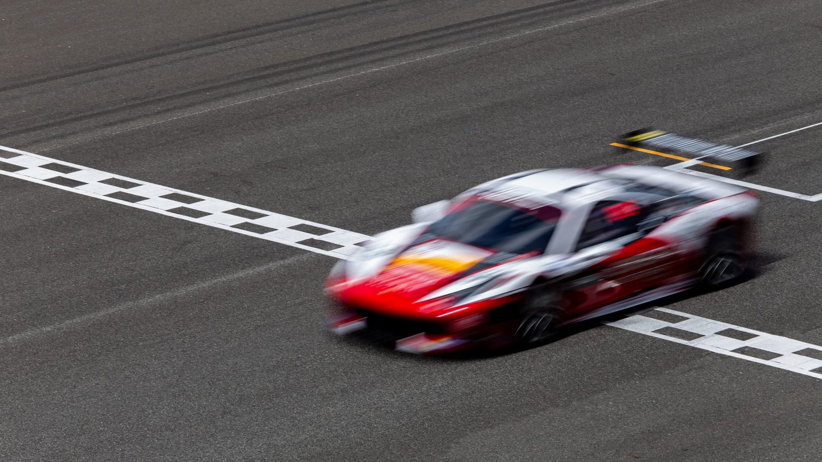 Voiture GT rouge et blanche floutée par la vitesse au moment de franchir la ligne d'arrivée à damier