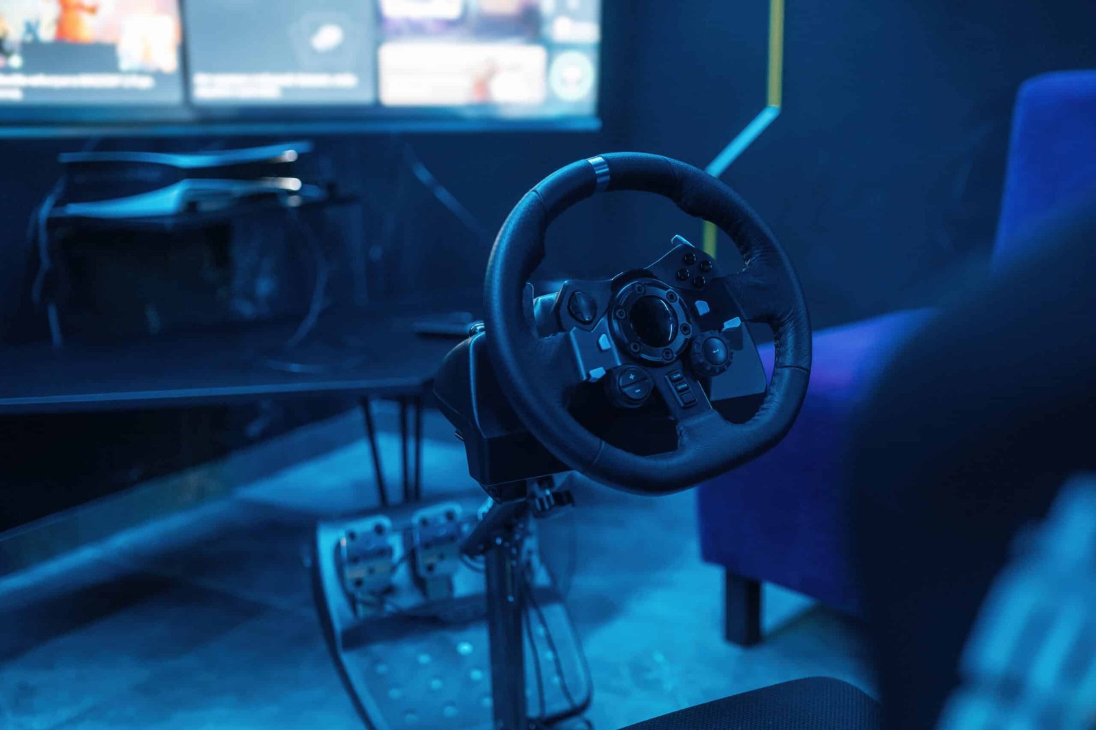 Volant simracing rond fixé au bord d'une table avec son pédalier au sol, pièce éclairée en bleu