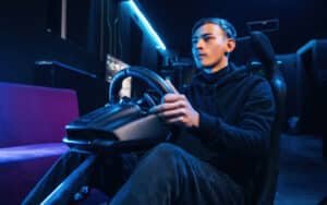 Pilote assis dans un baquet, une main sur un volant simracing fixé à un support, éclairage bleu et violet