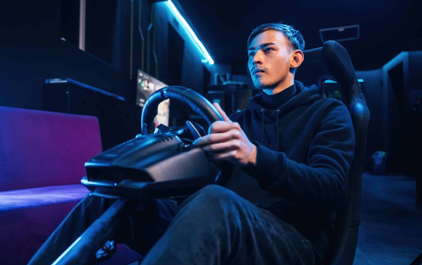 Pilote assis dans un baquet, une main sur un volant simracing fixé à un support, éclairage bleu et violet