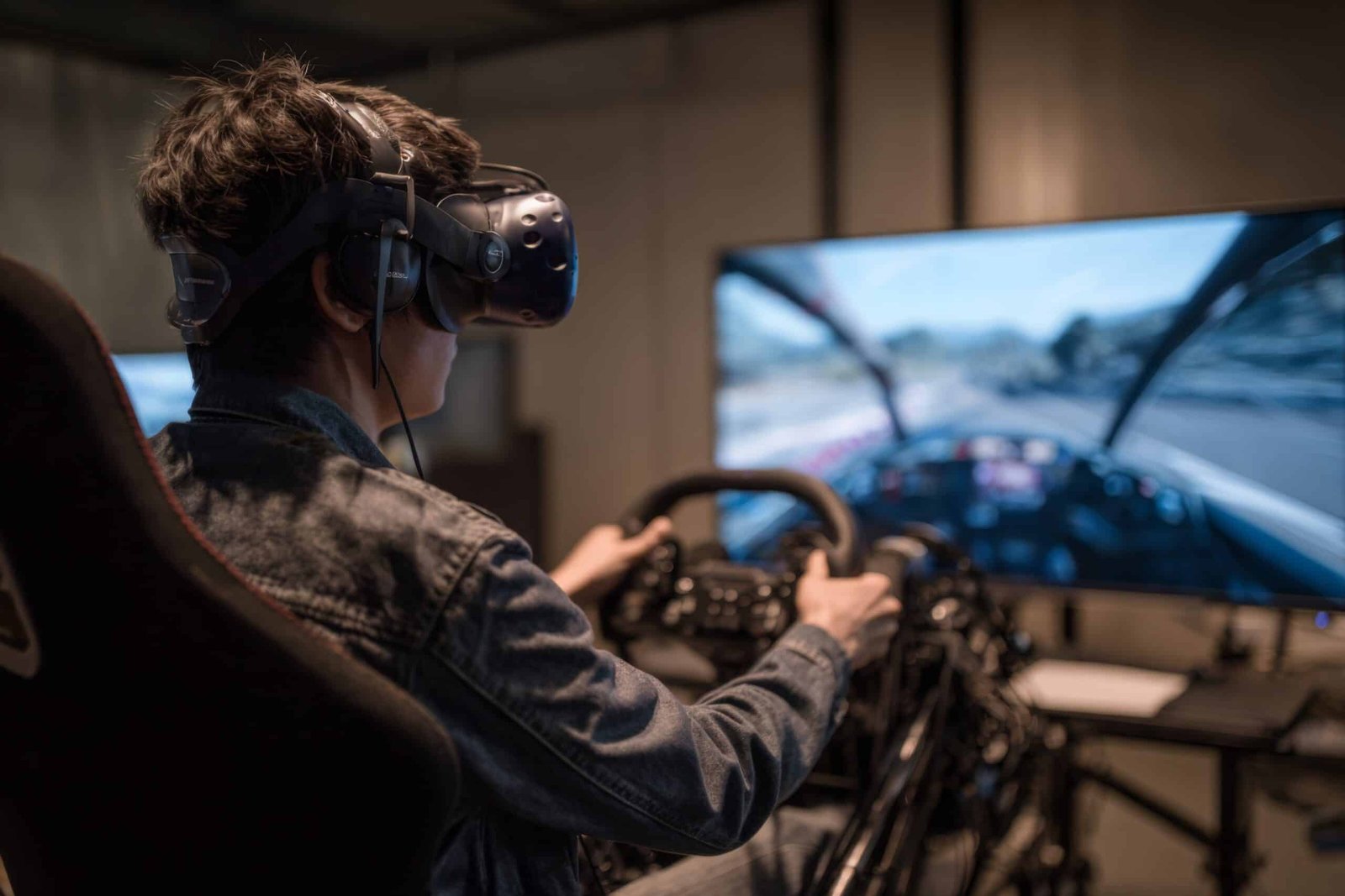Pilote portant un casque de réalité virtuelle au volant d'un simulateur, avec derrière lui un écran affichant une vue cockpit